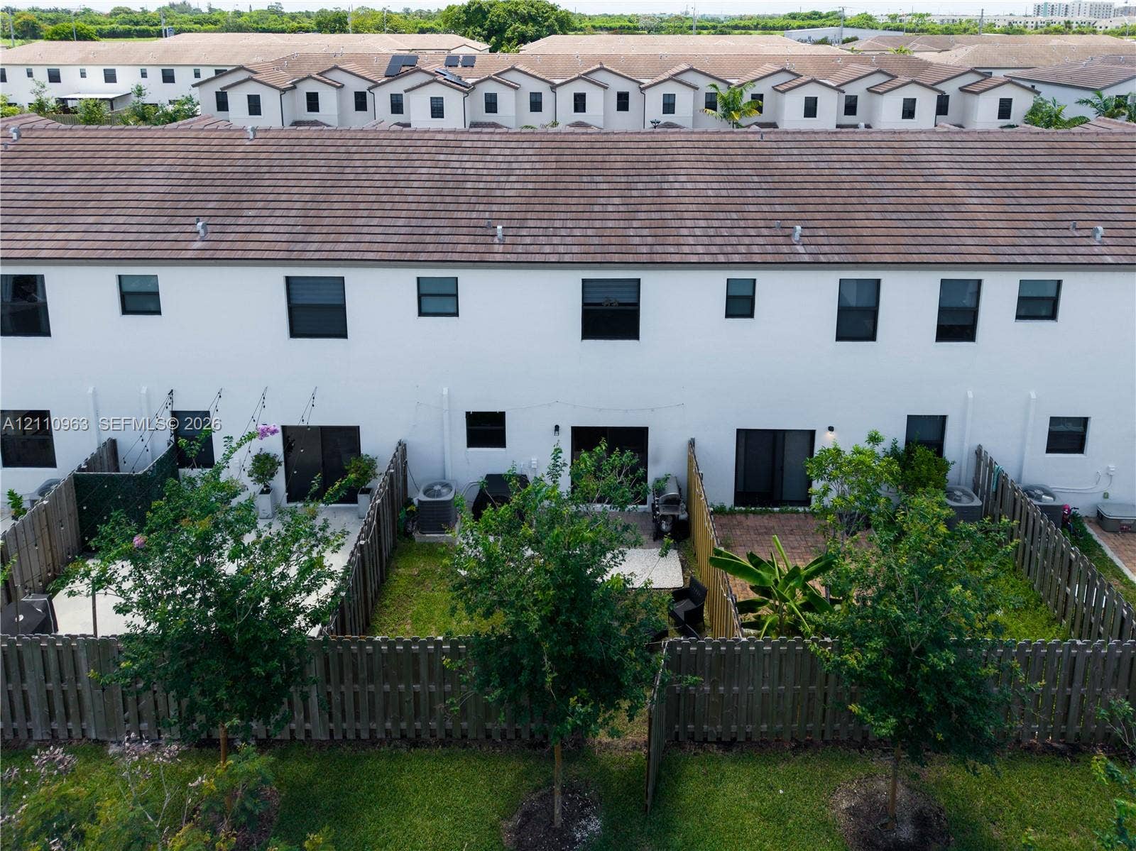 23436 SW 129th Avenue, #23436, Homestead, Homestead, FL 33032 Two-story townhome exterior featuring white stucco siding, a tiled roof, private fenced rear patios, and rear-entry sliding glass doors