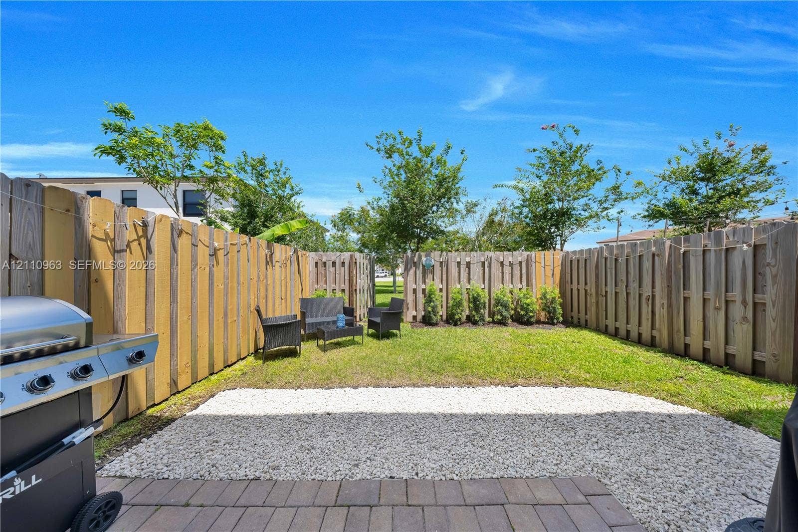23436 SW 129th Avenue, #23436, Homestead, Homestead, FL 33032 Private fenced backyard featuring a paved patio area, white stone ground cover, manicured lawn, and mature trees