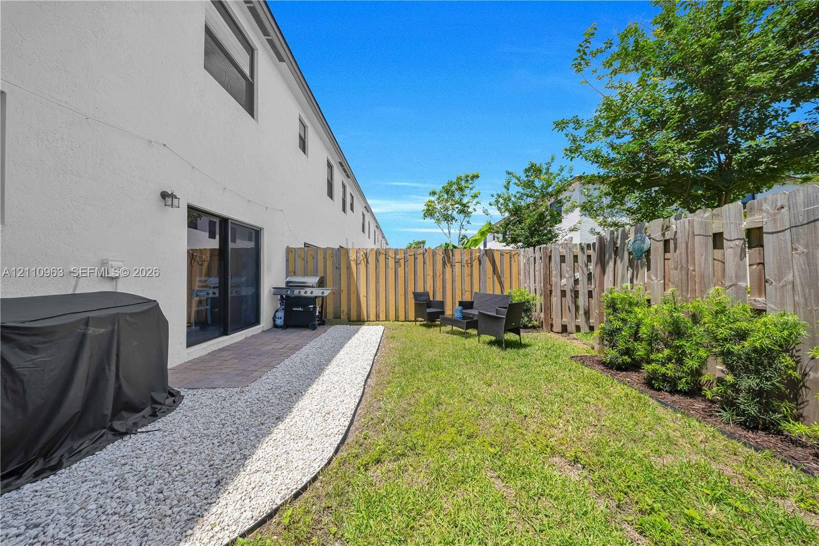 23436 SW 129th Avenue, #23436, Homestead, Homestead, FL 33032 Fenced backyard featuring a paver patio, stone-accented ground cover, established landscaping, and exterior wall-mounted lighting
