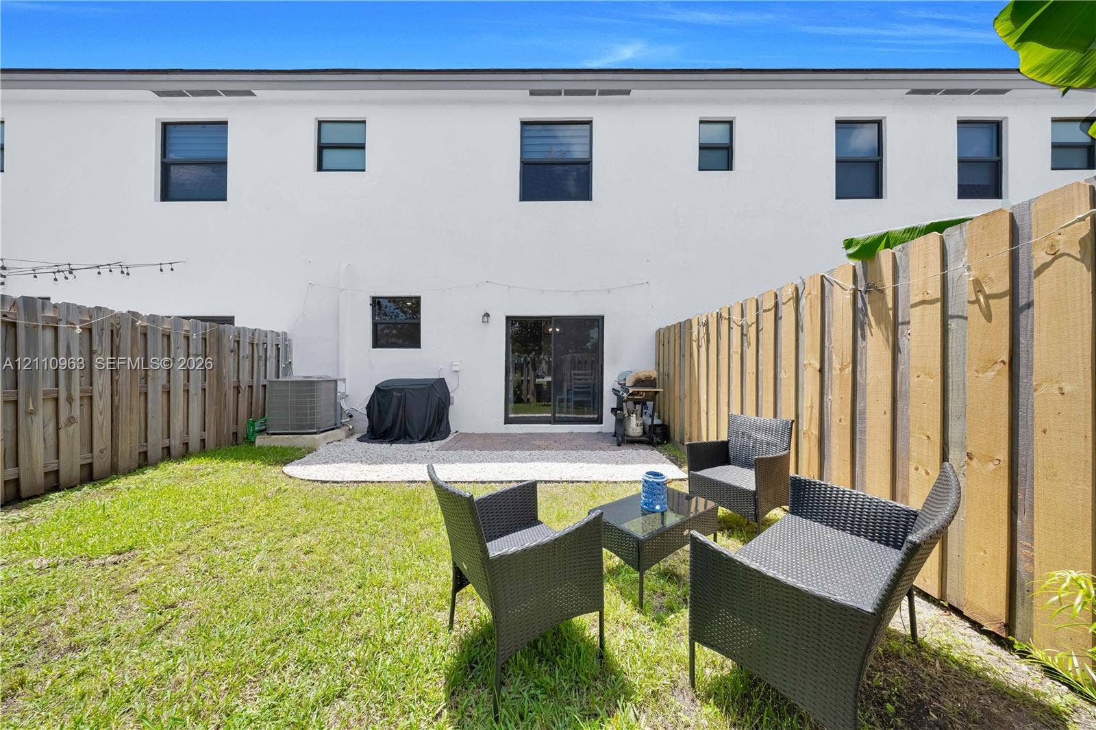 23436 SW 129th Avenue, #23436, Homestead, Homestead, FL 33032 Rear exterior featuring a smooth-stucco facade, a paved concrete patio, and a fully fenced yard with a manicured lawn