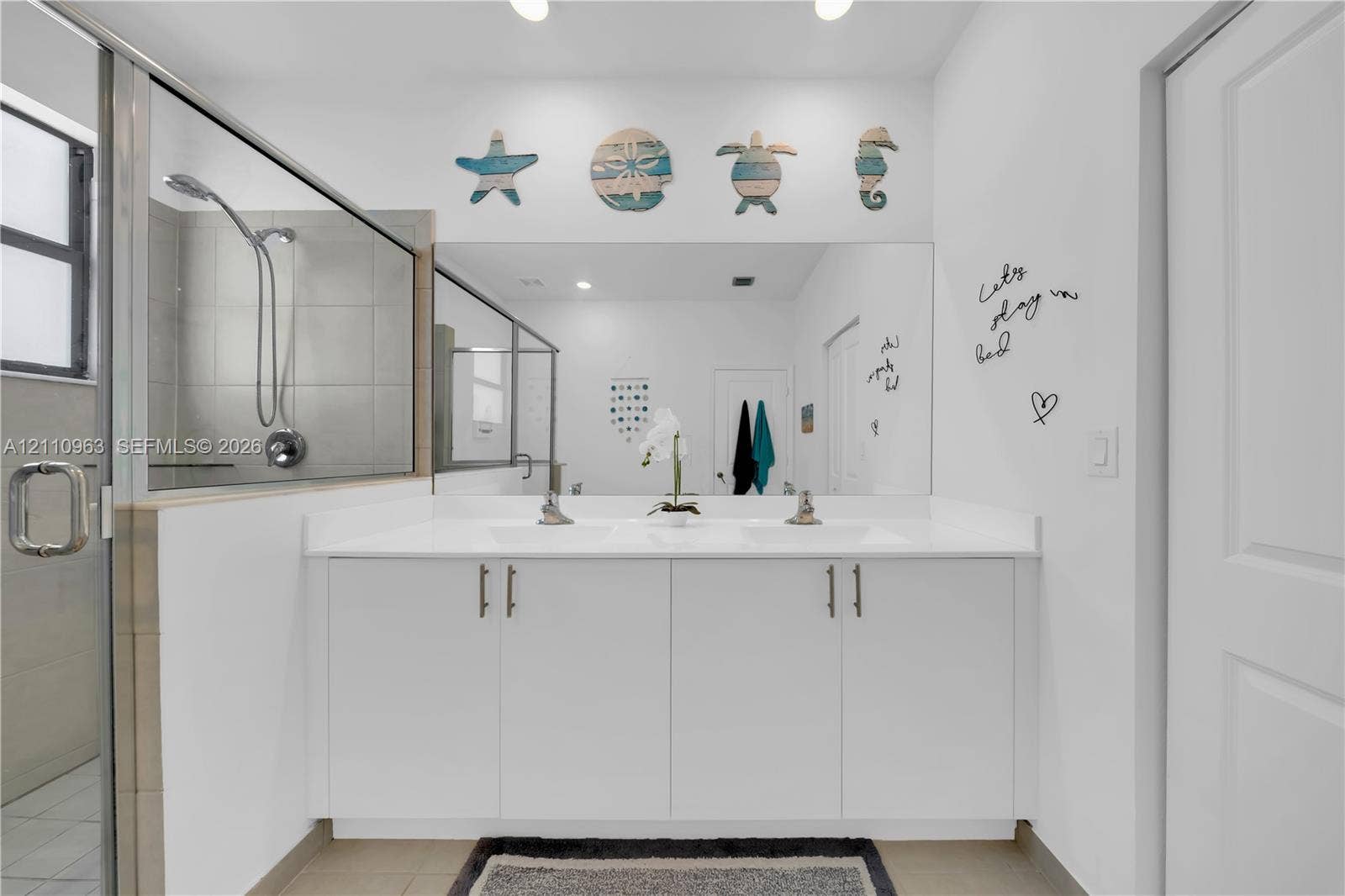 23436 SW 129th Avenue, #23436, Homestead, Homestead, FL 33032 Dual-sink vanity with white cabinetry, a solid-surface countertop, and a full-width mirror, paired with a glass-enclosed shower featuring tile surrounds and a wall-mounted showerhead