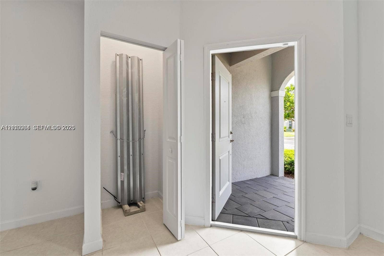 Entryway featuring large-format tile flooring, a storage closet, a white paneled door, and a tiled exterior porch with an arched architectural detail