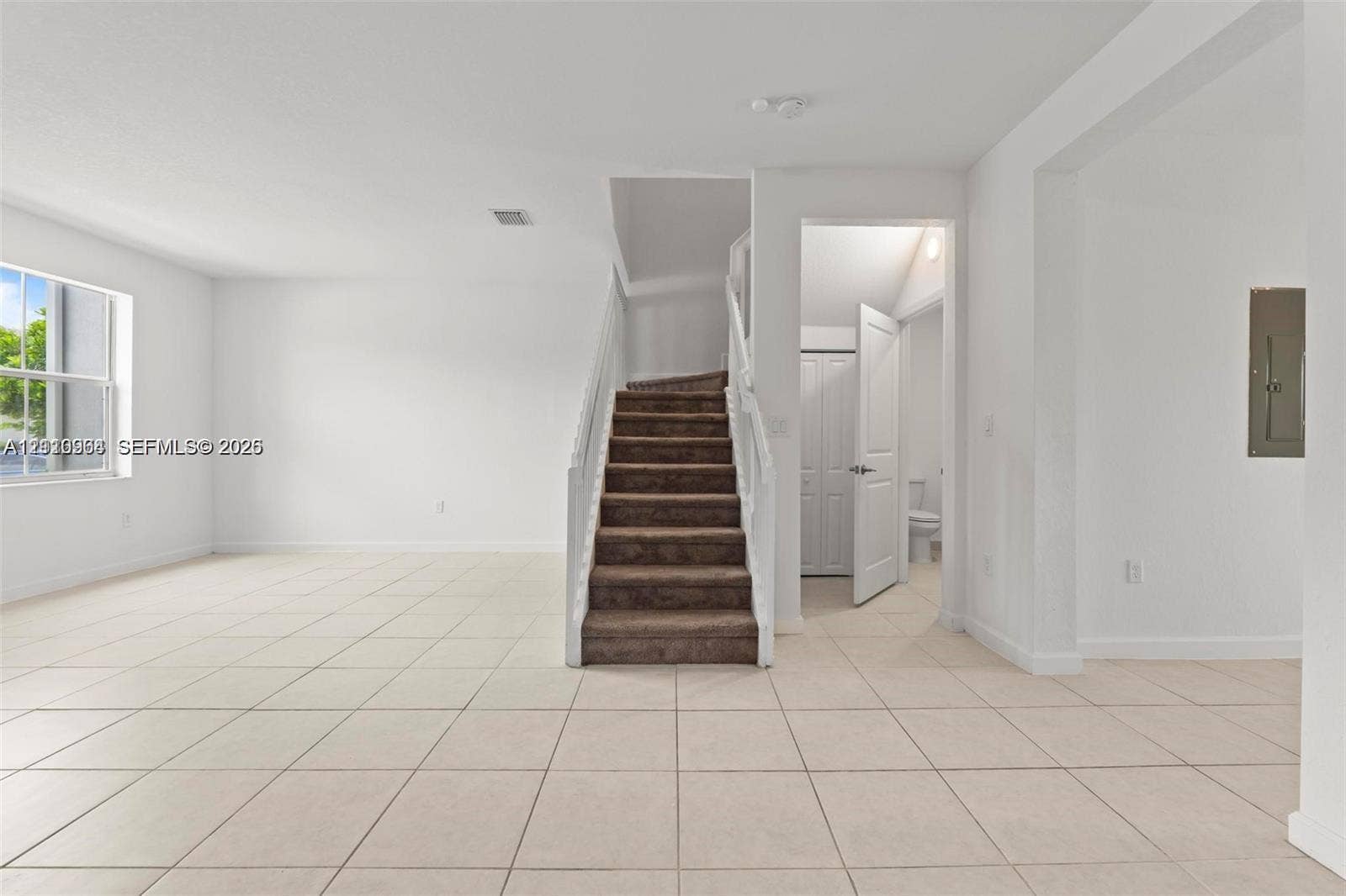 Open-concept floor plan featuring large-format ceramic tile flooring, a staircase with white painted balusters, and a single-hung window with natural light