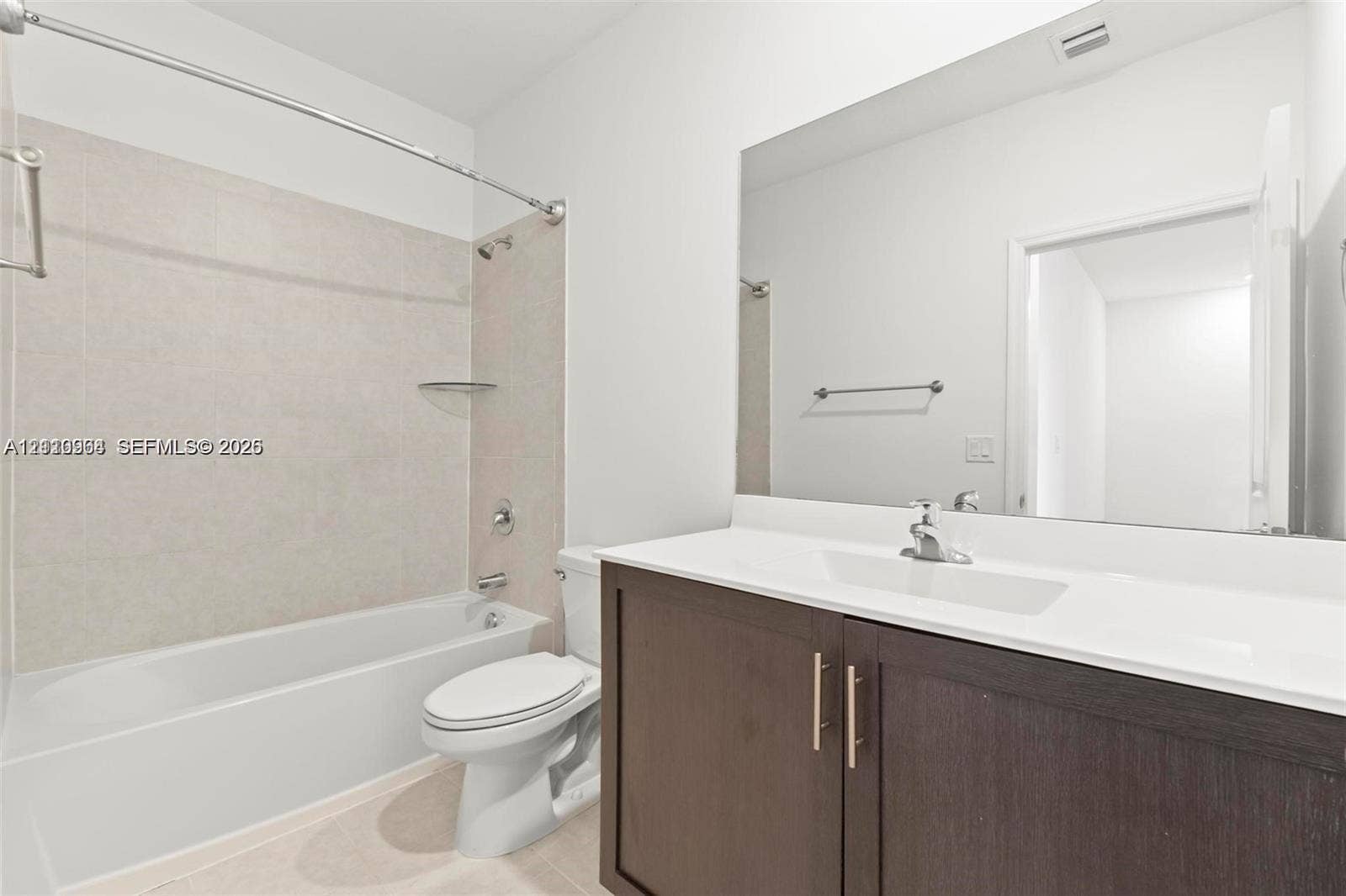 Bathroom featuring a dark wood-finish vanity with a white countertop, an integrated sink, an expansive wall-mounted mirror, and a tile-surround shower and tub combination