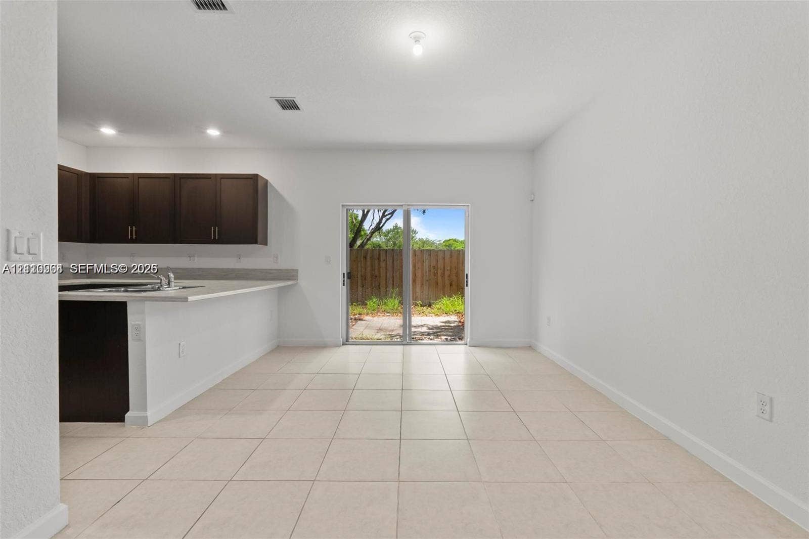 Open-concept interior featuring light-toned tile flooring, dark cabinetry, solid-surface countertops, and sliding glass doors with exterior access