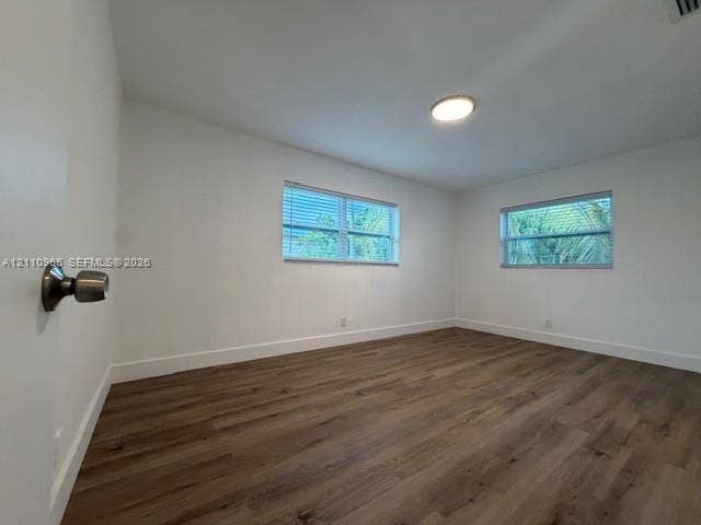 Interior room featuring wood-finish flooring, two windows with horizontal blinds, and a flush-mount ceiling light fixture