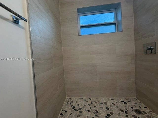 Walk-in shower enclosure featuring large-format neutral-tone tile walls, river stone flooring, an integrated rectangular window, and polished chrome fixtures