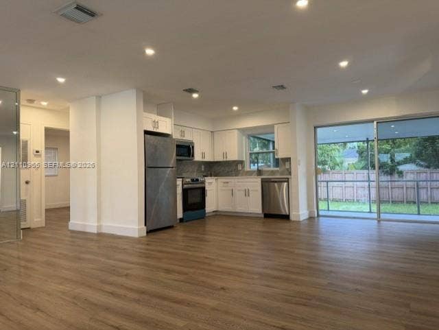 Kitchen featuring white shaker-style cabinetry, stainless steel appliances, and wood-finish flooring, accompanied by recessed lighting and a sliding glass door