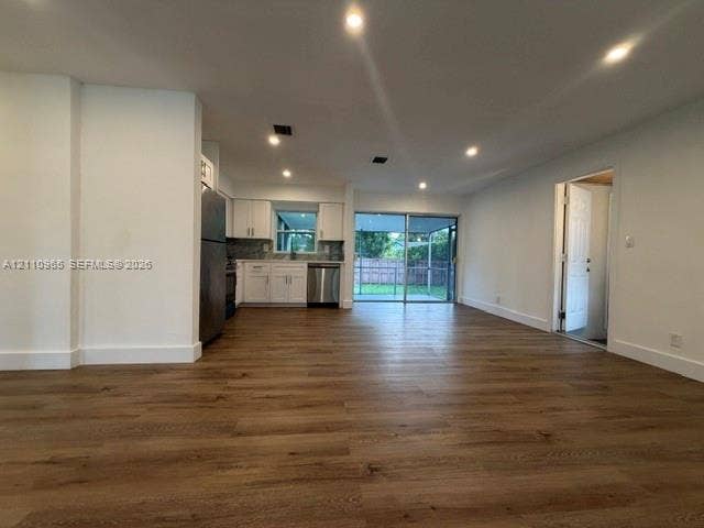 Open-concept interior featuring wood-finish flooring, recessed lighting, white cabinetry, stainless steel appliances, and sliding glass doors