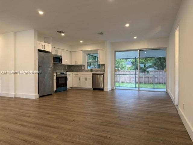 Kitchen featuring white cabinetry, stainless steel appliances, and stone-finish countertops, completed by wood-finish flooring and floor-to-ceiling sliding glass doors