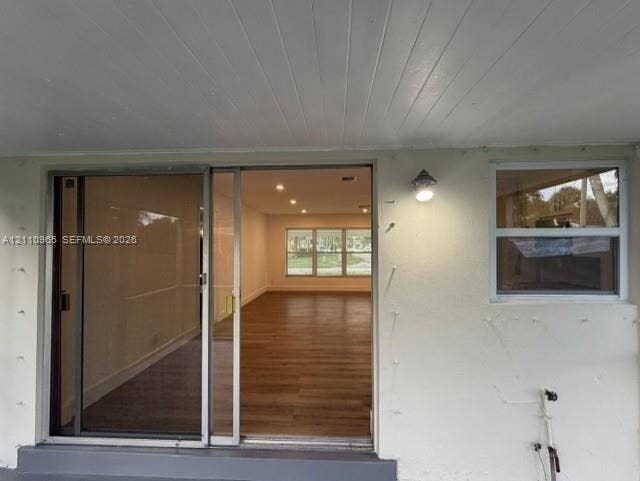 Covered exterior entryway featuring a sliding glass door, single-pane window, recessed ceiling lighting, and wood-finish flooring visible within the interior