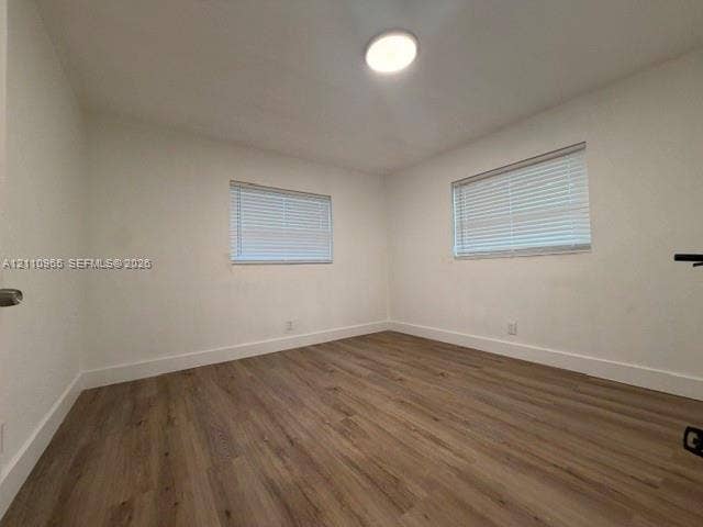 Room featuring wood-finish flooring, two windows with horizontal blinds, and a flush-mount ceiling light fixture