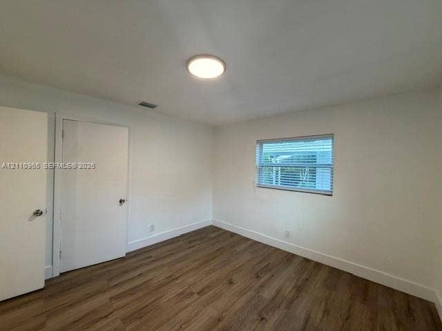 Room featuring wood-finish flooring, white walls, two interior doors, and a window with horizontal blinds