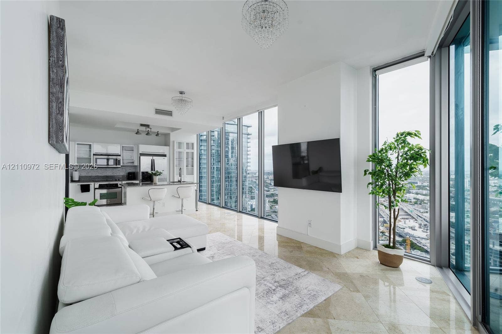 Floor-to-ceiling windows, polished stone tile flooring, stainless steel appliances, white cabinetry, and crystal-style chandelier lighting