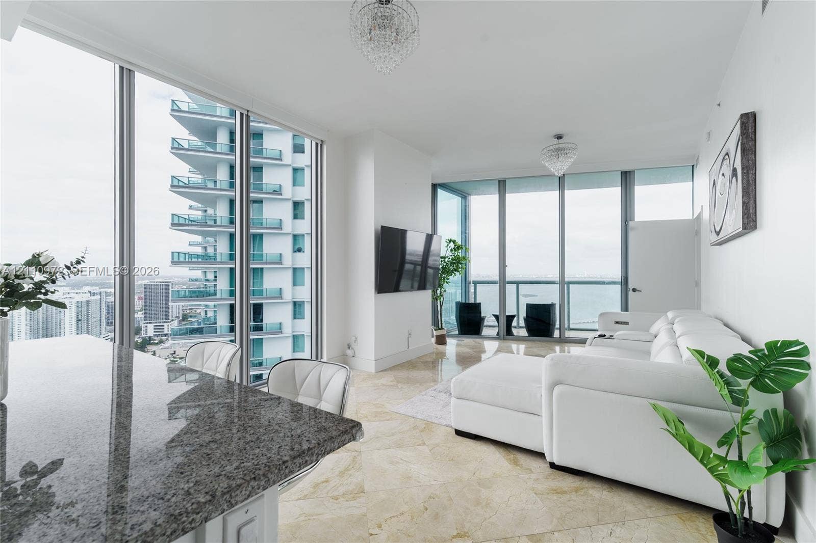 Floor-to-ceiling windows, natural stone flooring, dual crystal chandeliers, and expansive glass balcony enclosure