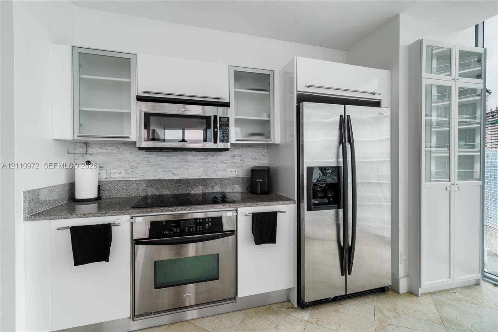 Kitchen featuring high-gloss white cabinetry, stone-finish countertops, tile backsplash, built-in stainless steel appliances, and glass-front display cabinetry