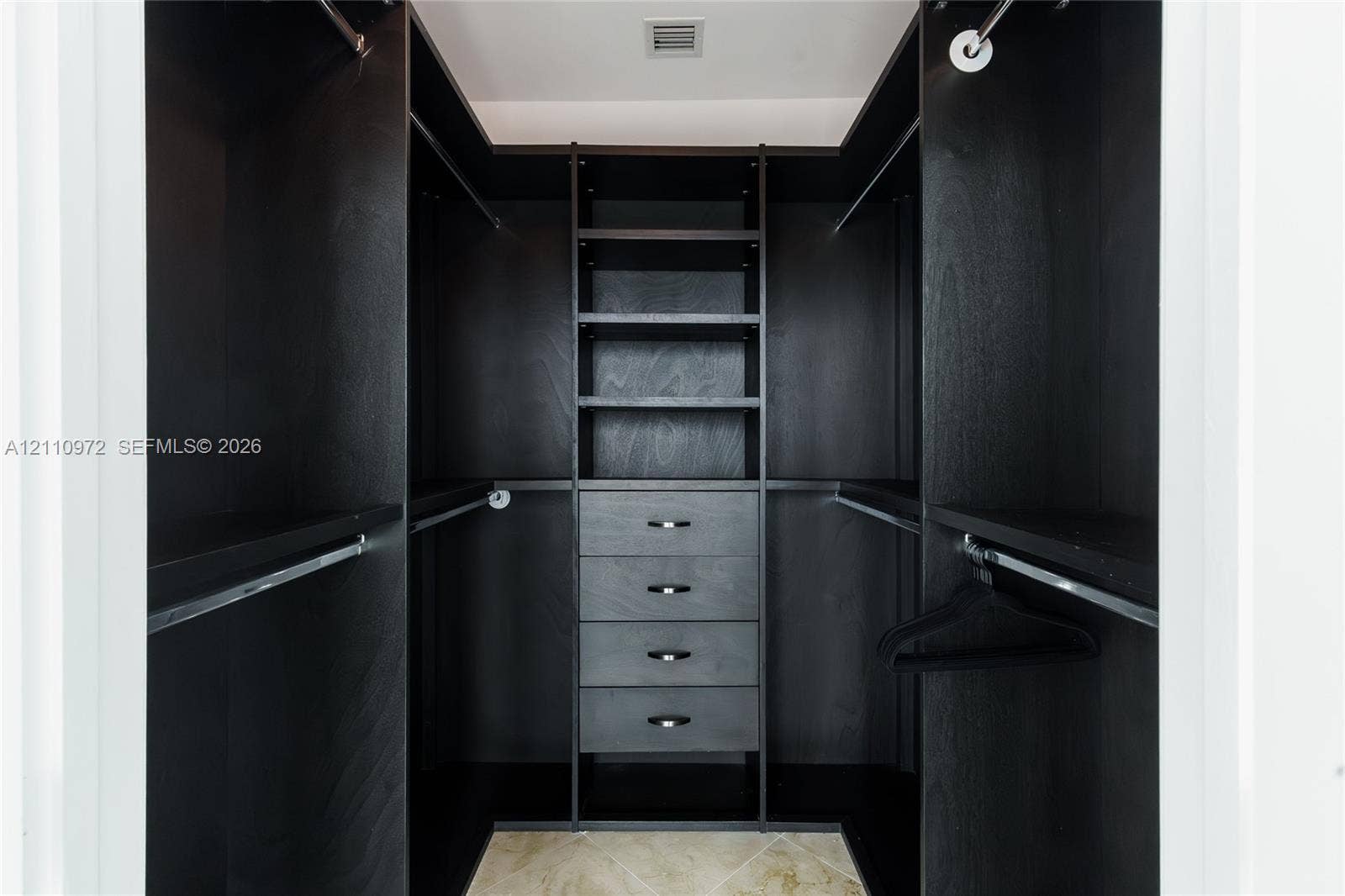 Custom walk-in closet featuring dark wood-finish cabinetry, built-in shelving, four integrated storage drawers, and polished metal hardware