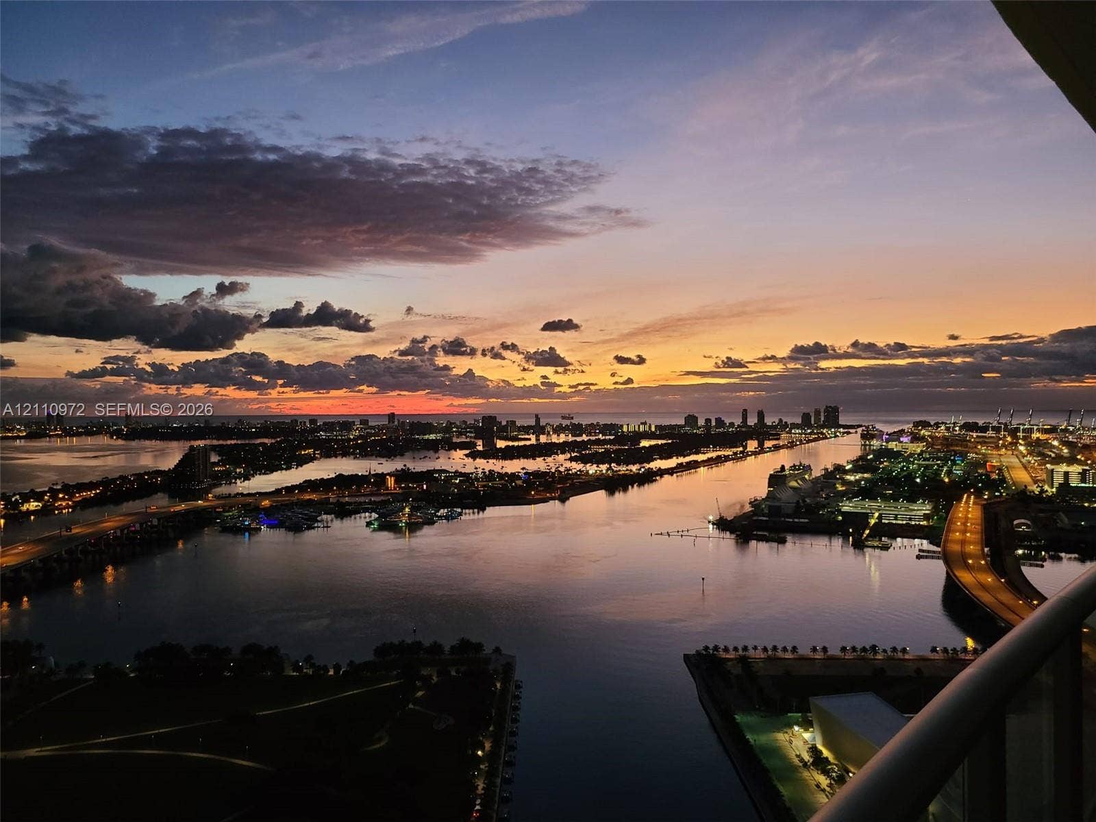 Elevated balcony featuring a panoramic cityscape, waterfront scenery, and horizon sunset