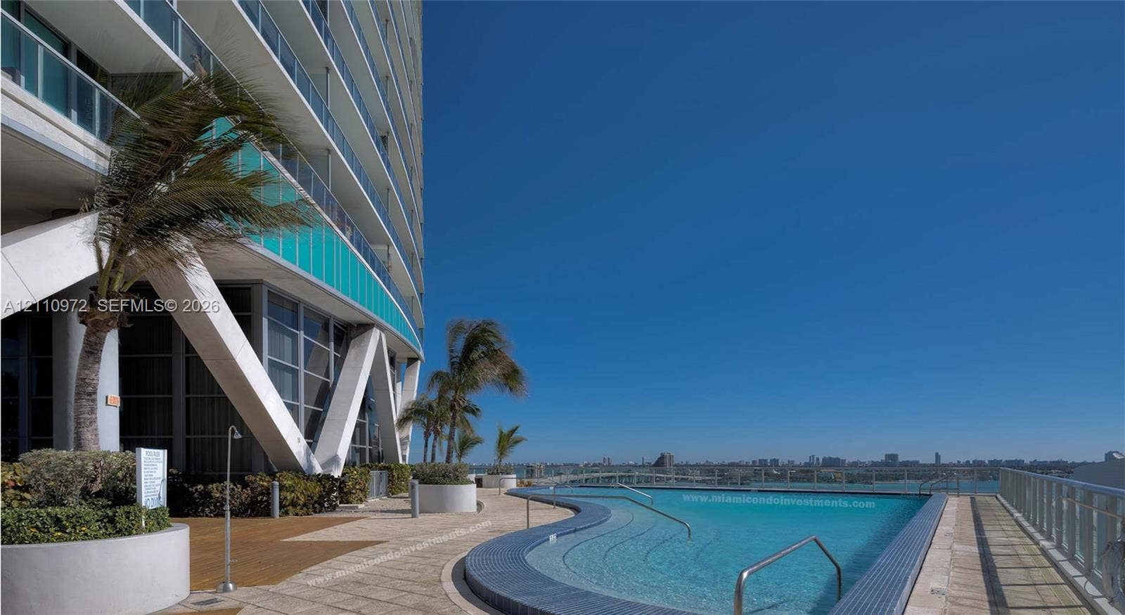 Outdoor pool featuring a curved tiled edge, tile decking, integrated tiered steps, and metal railings, set against an architectural facade with structural support beams and glass balcony partitions