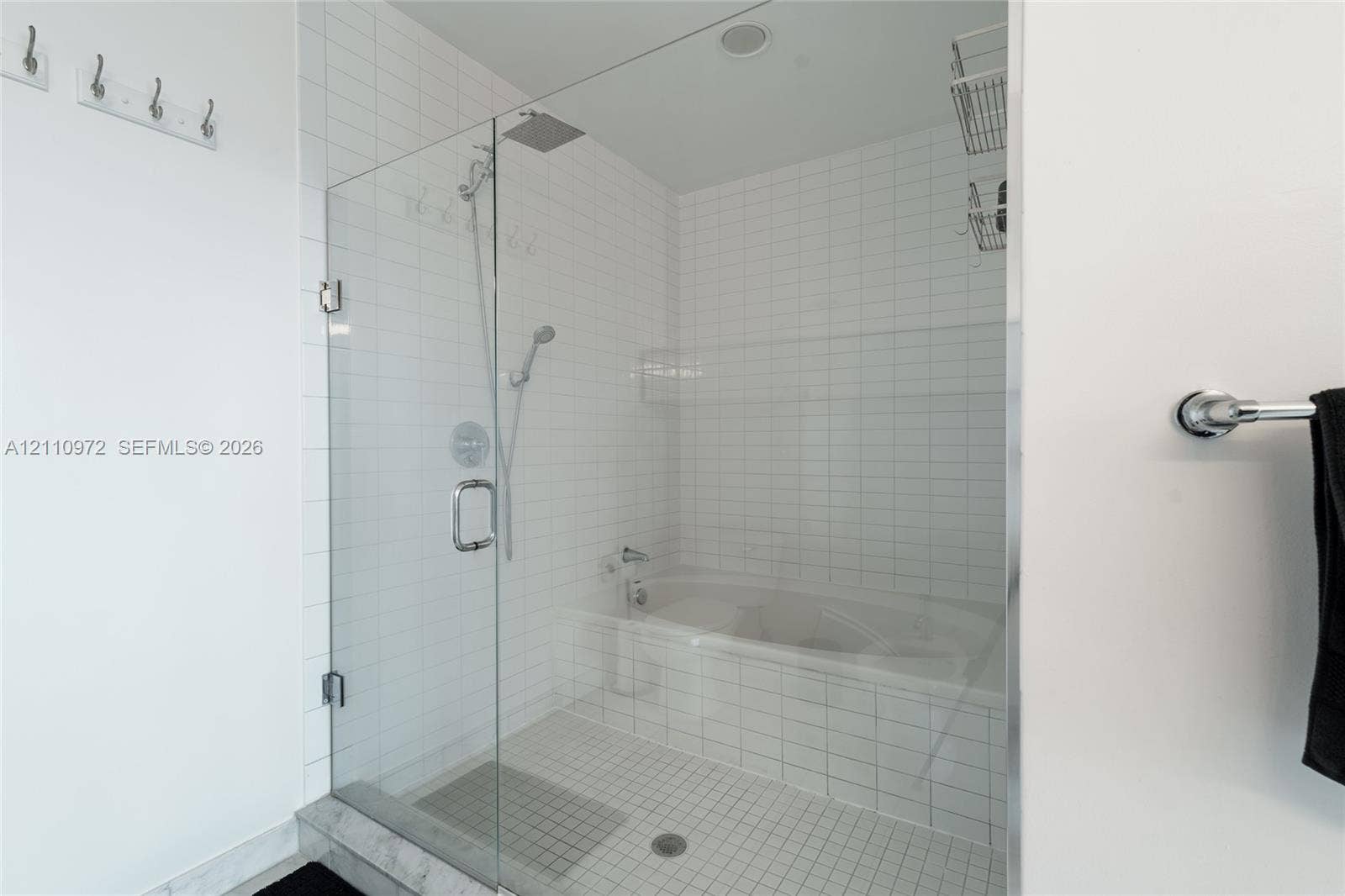 Walk-in shower with frameless glass door, soaking tub, square white wall tiling, rain-style shower head, and chrome fixtures