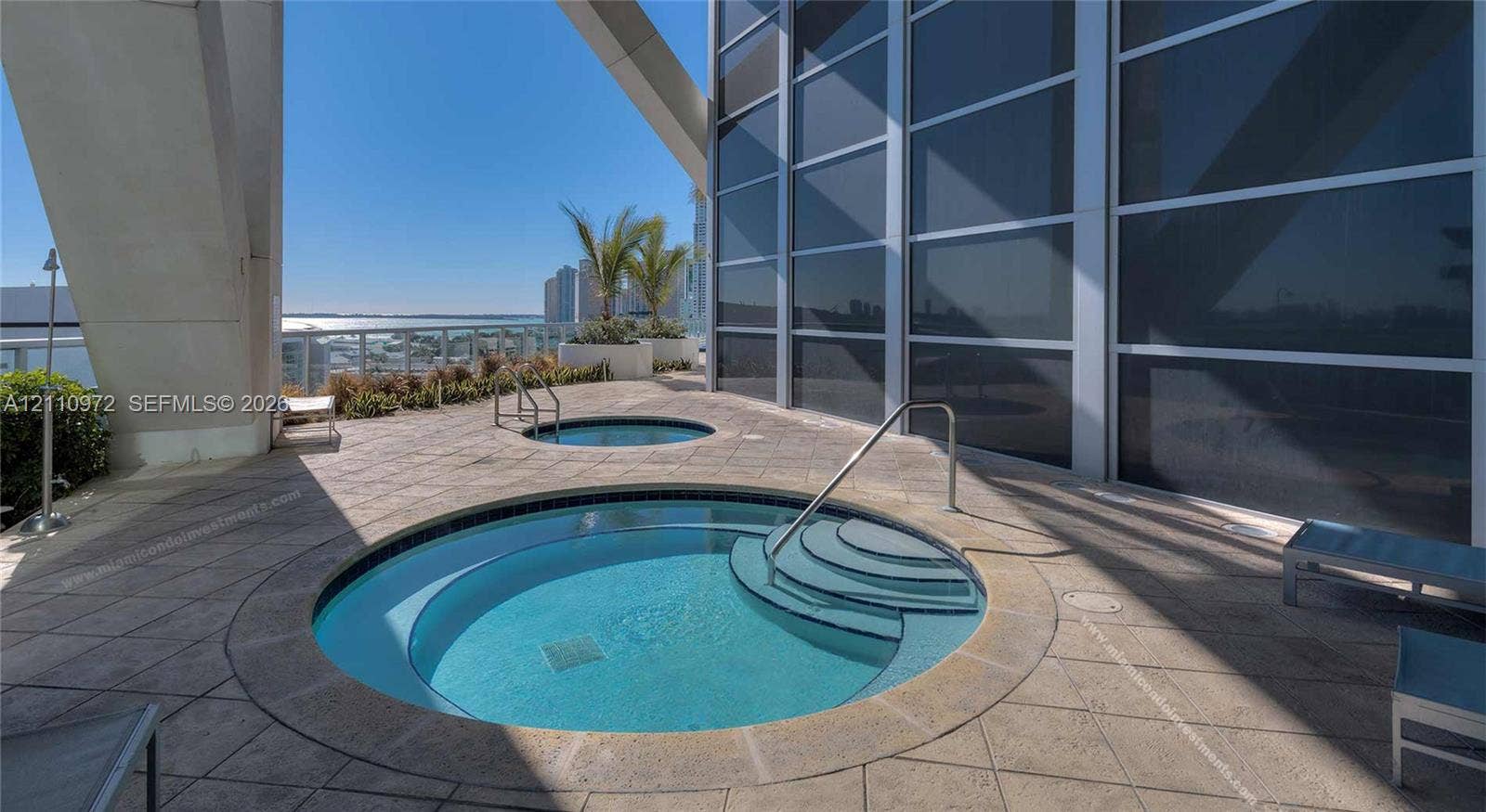 Terrace featuring two circular in-ground spas, stone-paver flooring, metal handrails, and floor-to-ceiling glass paneling