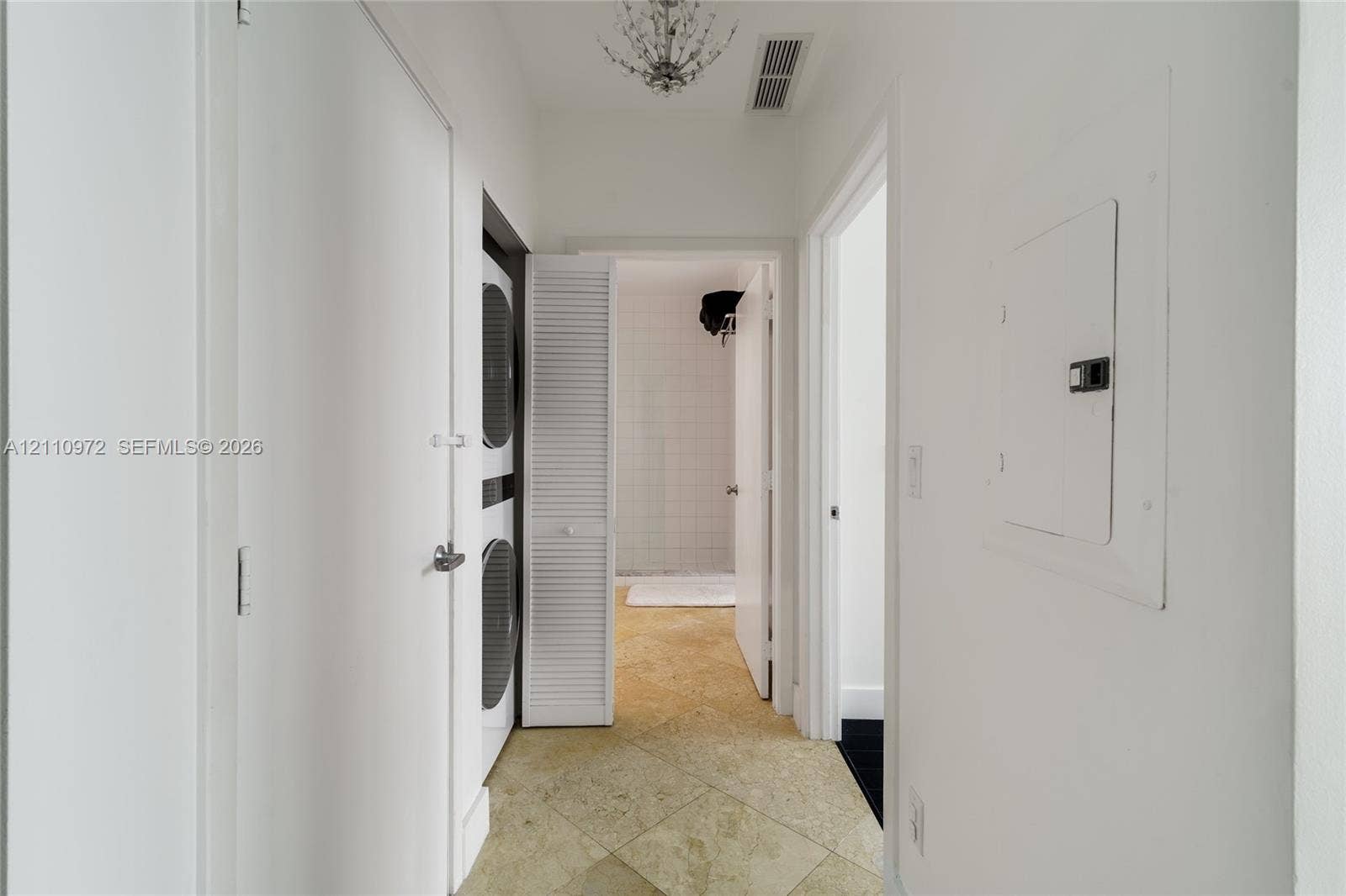 Hallway featuring stone-finish tile flooring, a decorative ceiling-mounted chandelier, and an integrated laundry closet with louvered doors