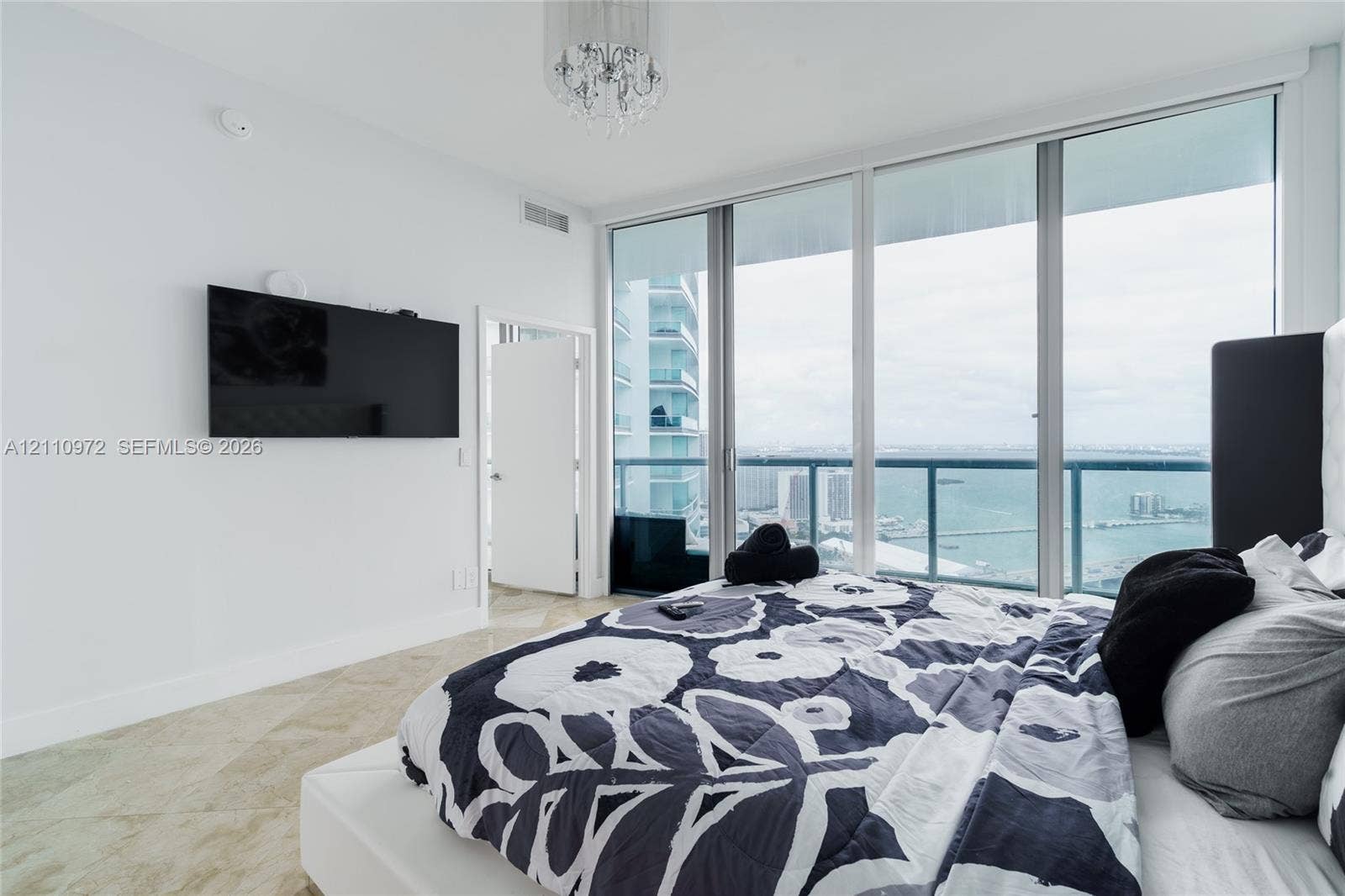Floor-to-ceiling windows, natural stone flooring, crystal chandelier, and balcony access with water scenery