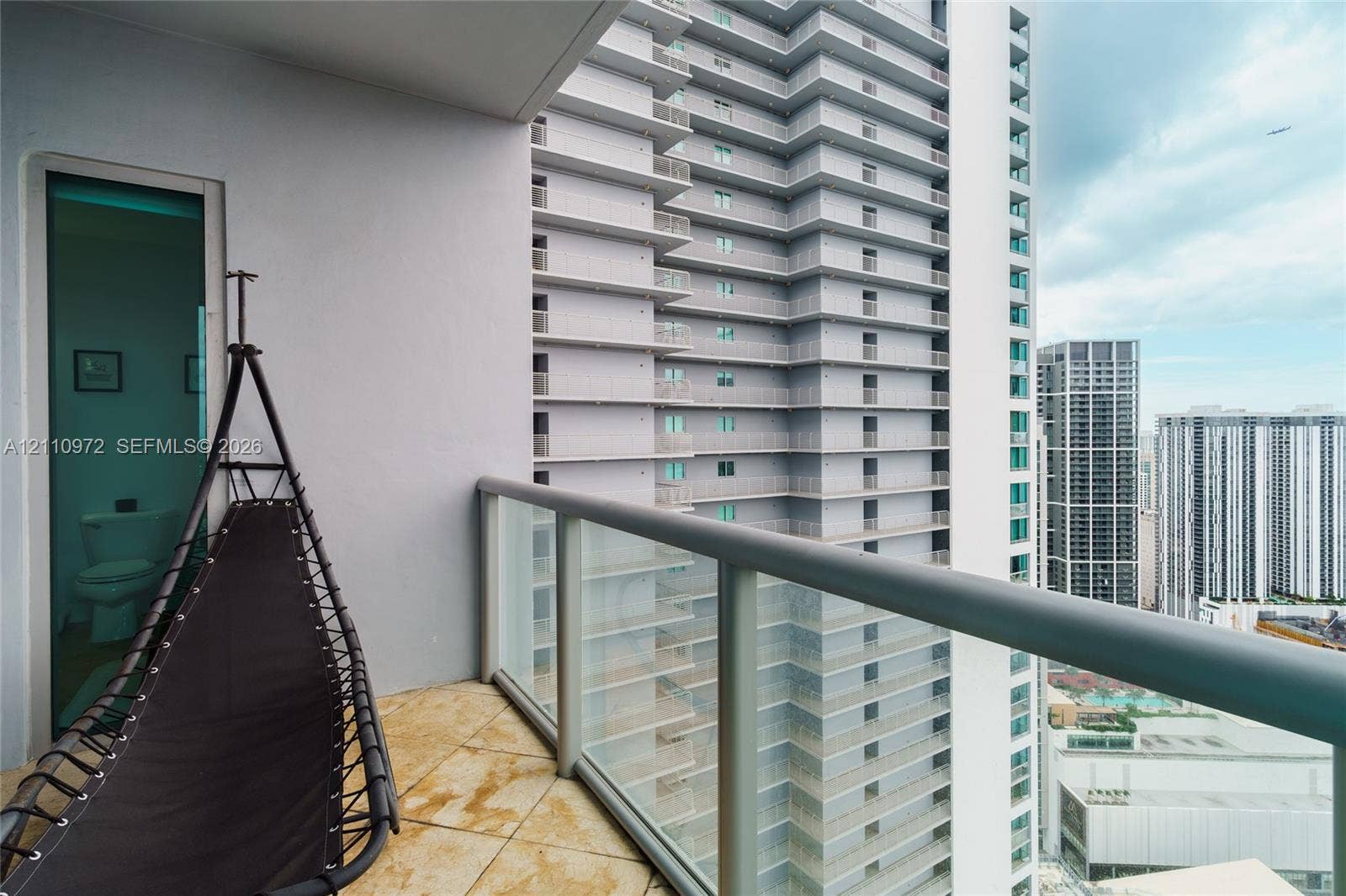 Covered balcony featuring tile flooring and a glass-panel railing with metal frame
