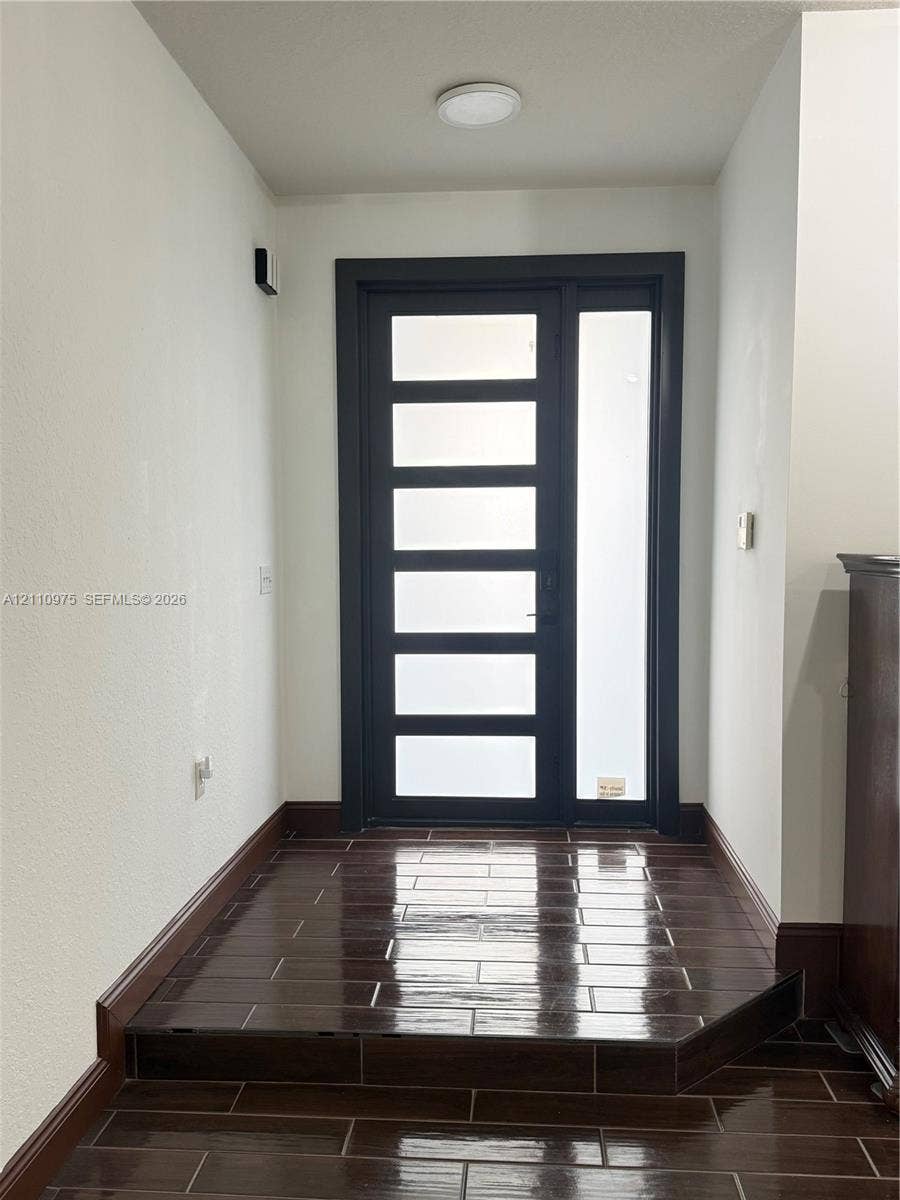 2030 NW 99th Terrace, Pembroke Pines, FL 33024 Modern entry featuring a dark-framed door with multi-panel glass inserts, a matching full-length glass sidelight, and dark-toned rectangular tile flooring