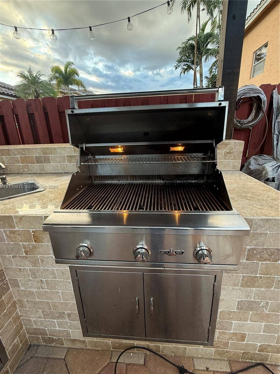 2030 NW 99th Terrace, Pembroke Pines, FL 33024 Outdoor kitchen featuring a built-in stainless steel grill, natural stone masonry surround, integrated stainless steel storage cabinet, and an inset sink