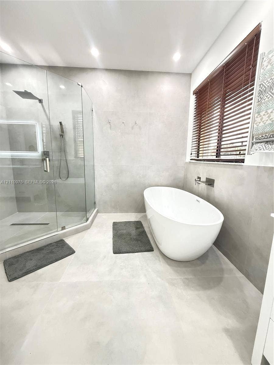 2030 NW 99th Terrace, Pembroke Pines, FL 33024 Freestanding oval soaking tub with wall-mounted faucet, walk-in glass-enclosed shower, large-format tile wall and floor surfaces, and recessed ceiling lighting