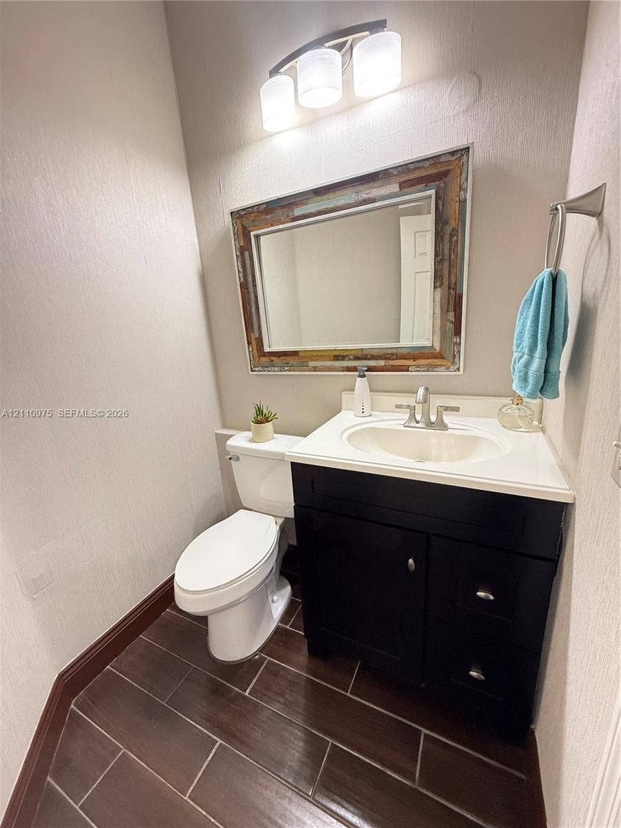 2030 NW 99th Terrace, Pembroke Pines, FL 33024 Dark-toned cabinetry with a white integrated countertop, wood-finish tile flooring, three-light vanity fixture, and brushed metal hardware