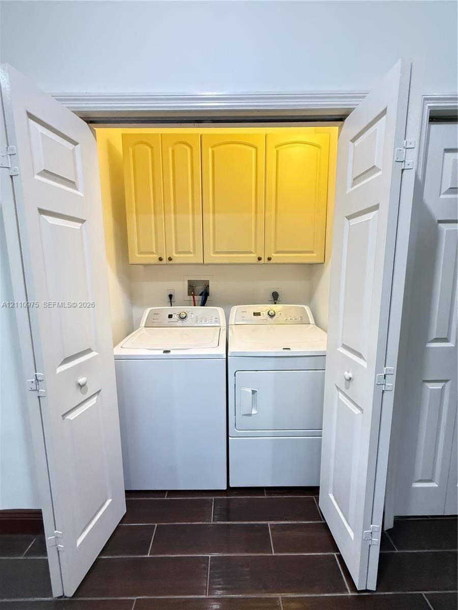 2030 NW 99th Terrace, Pembroke Pines, FL 33024 Laundry closet featuring white bi-fold doors, upper cabinet storage with raised-panel doors, and tile flooring