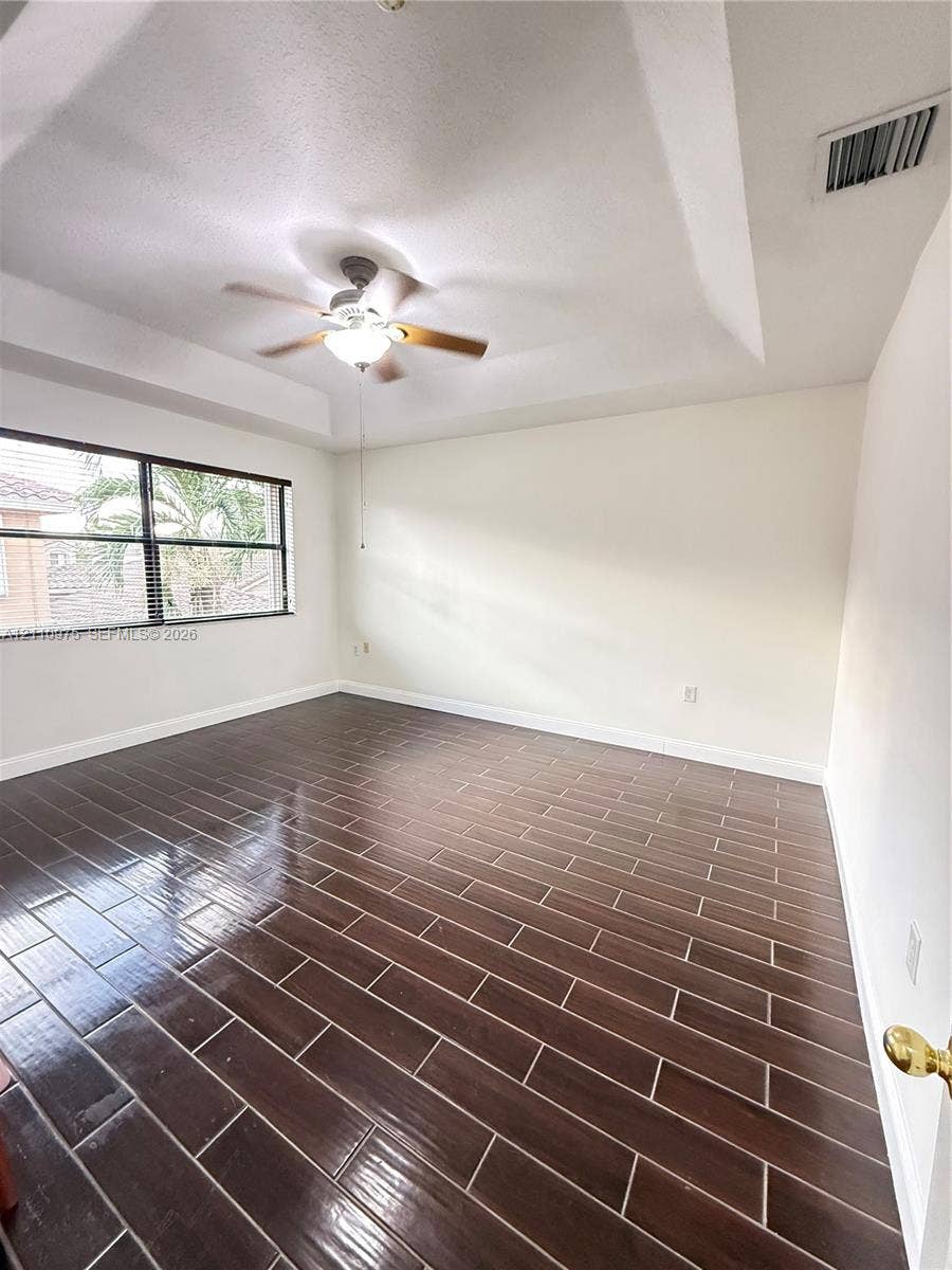 2030 NW 99th Terrace, Pembroke Pines, FL 33024 Tray ceiling with central mounted ceiling fan and light fixture, large-format dark wood-finish tile flooring, and oversized window with horizontal blinds