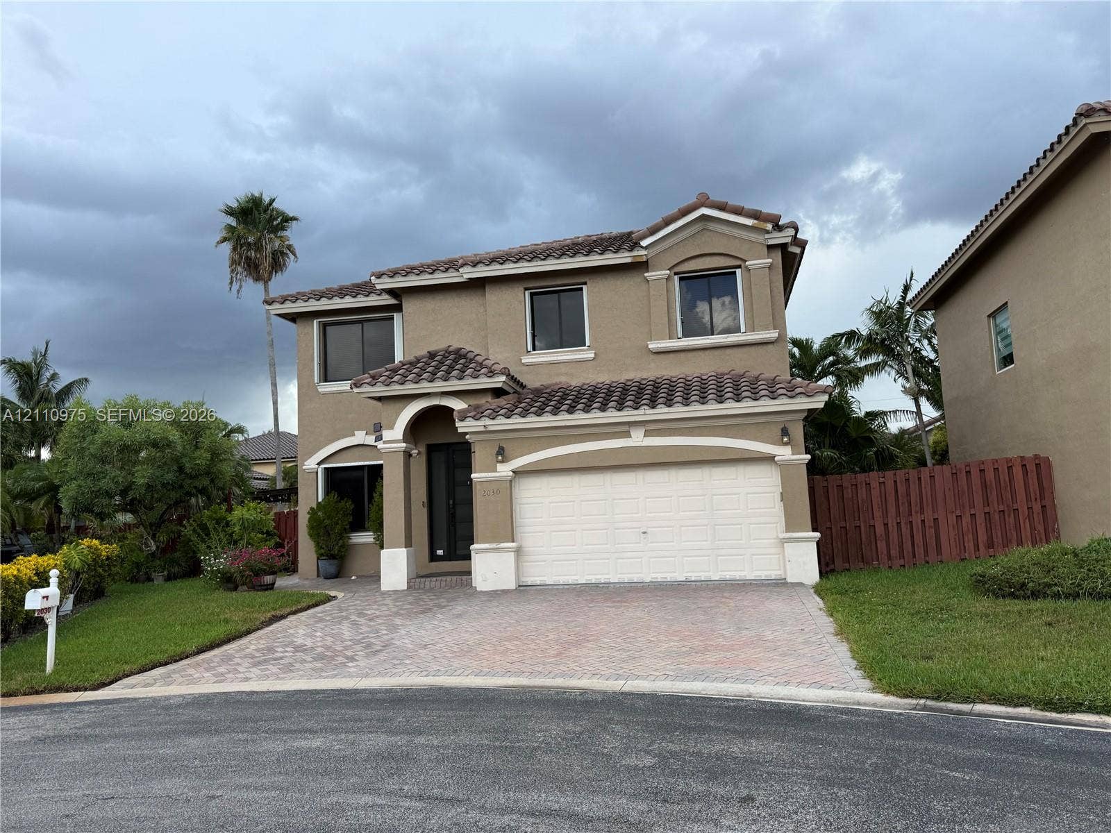 2030 NW 99th Terrace, Pembroke Pines, FL 33024 Two-story residence featuring a terracotta-tiled roof, stucco exterior, decorative archway at the main entrance, and a paved stone driveway leading to an attached two-car garage
