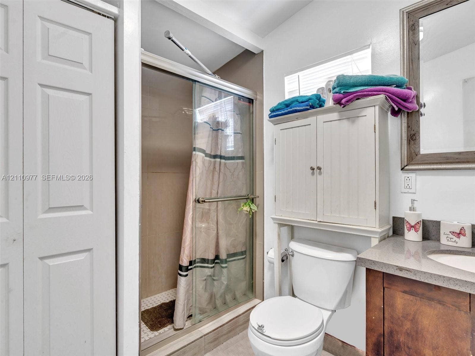 2126 Cleveland Street, #2126, Hollywood, Hollywood, FL 33020 Bathroom featuring a shower stall with a glass door, wood-tone vanity with a solid-surface countertop, integrated basin, and an over-the-toilet storage cabinet