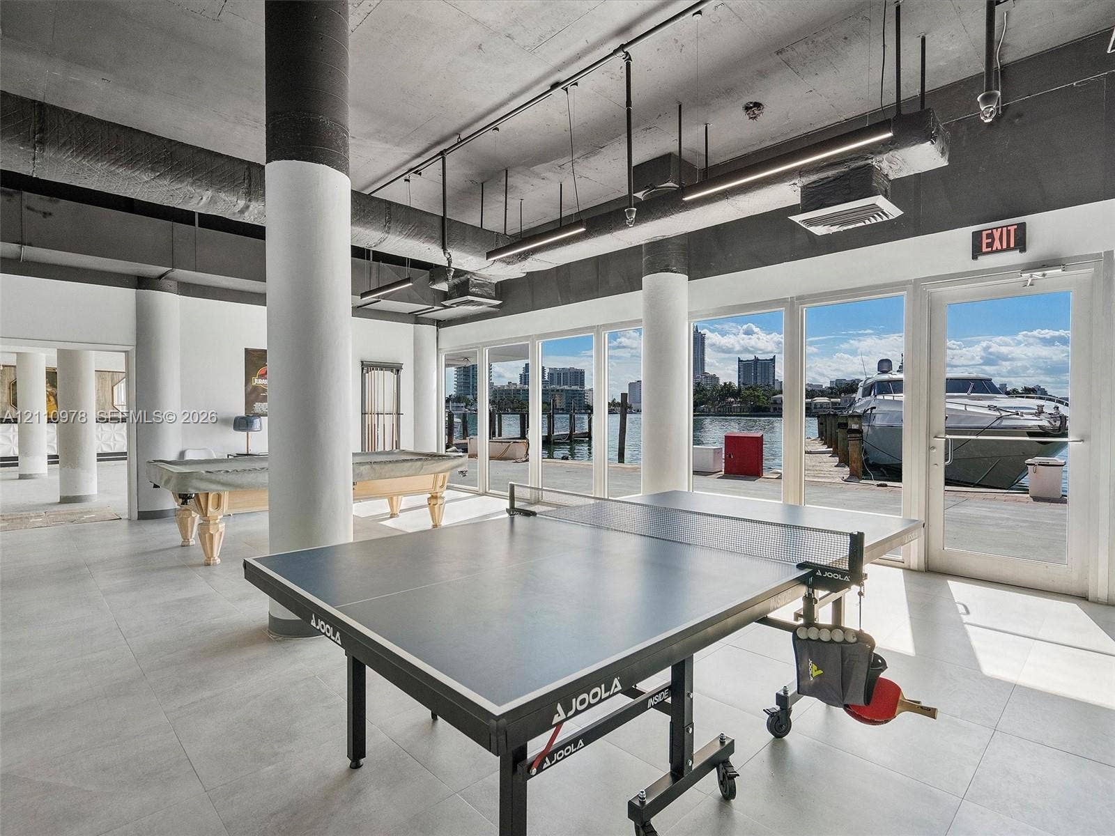 900 Bay Drive, #225, Miami Beach, FL 33141 Open-concept interior featuring exposed concrete ceilings, cylindrical structural columns, large-format tile flooring, and floor-to-ceiling glass paneling with direct water access