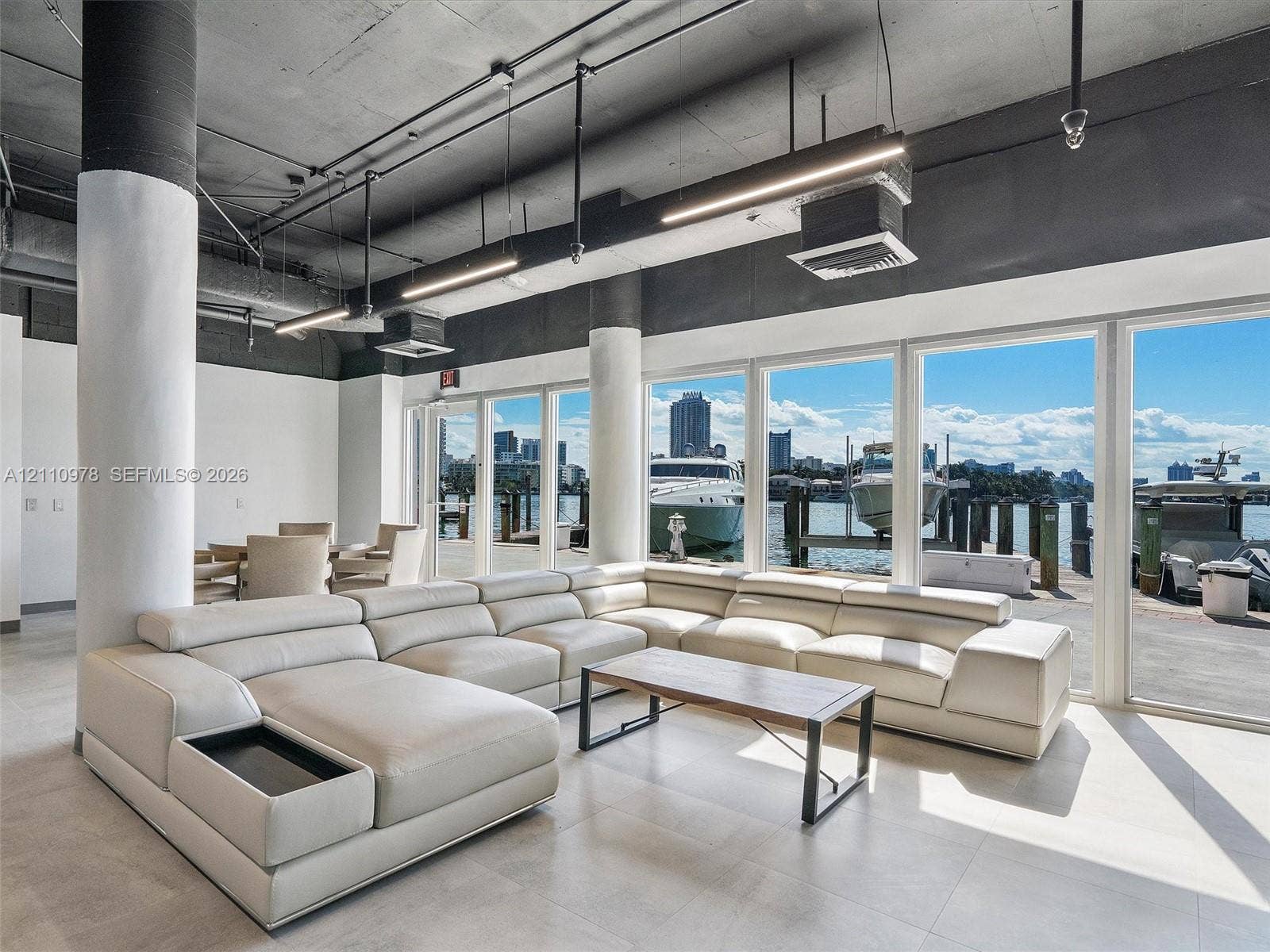 900 Bay Drive, #225, Miami Beach, FL 33141 Industrial-style interior featuring exposed concrete ceilings, cylindrical structural columns, expansive floor-to-ceiling windows, and large-format tile flooring