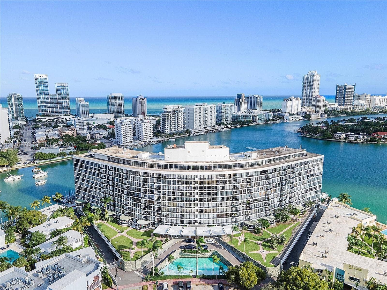 900 Bay Drive, #225, Miami Beach, FL 33141 Waterfront high-rise building featuring extensive balconies, a circular architectural design, a ground-level swimming pool, and manicured landscaping