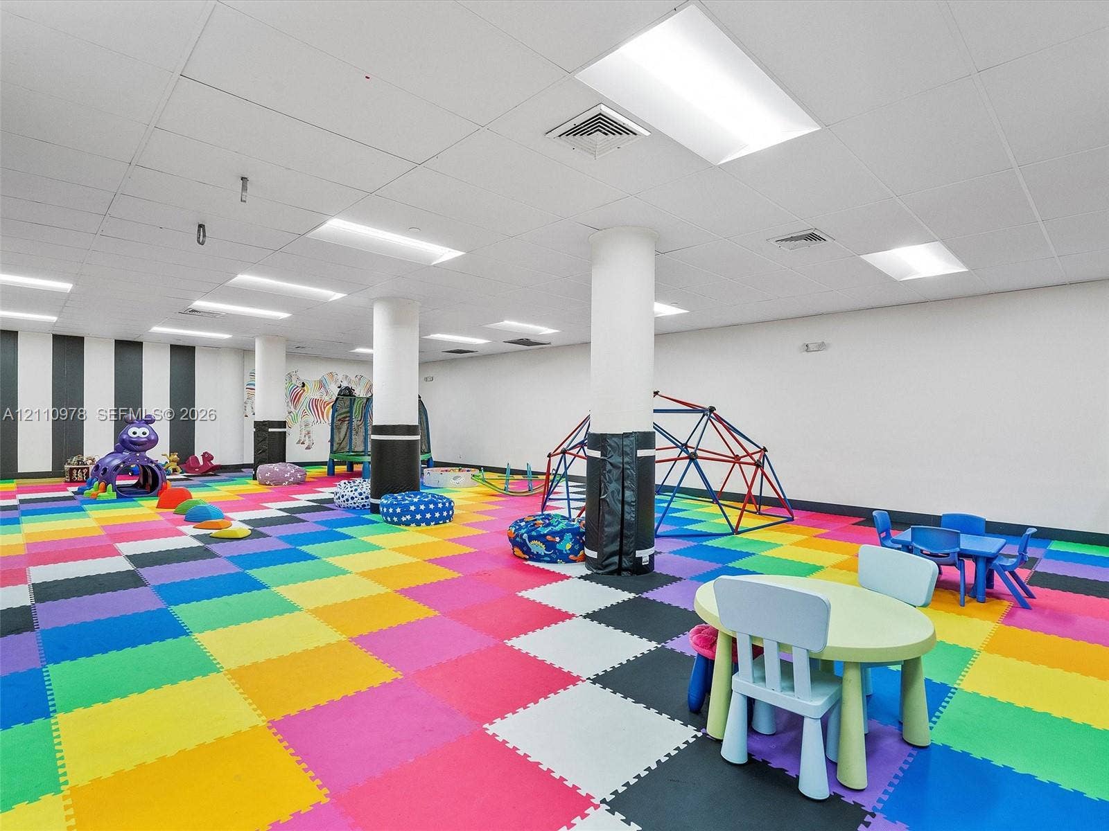 900 Bay Drive, #225, Miami Beach, FL 33141 Open-concept interior space featuring high-contrast wall accents, modular foam flooring, structural support pillars with protective padding, and recessed overhead lighting