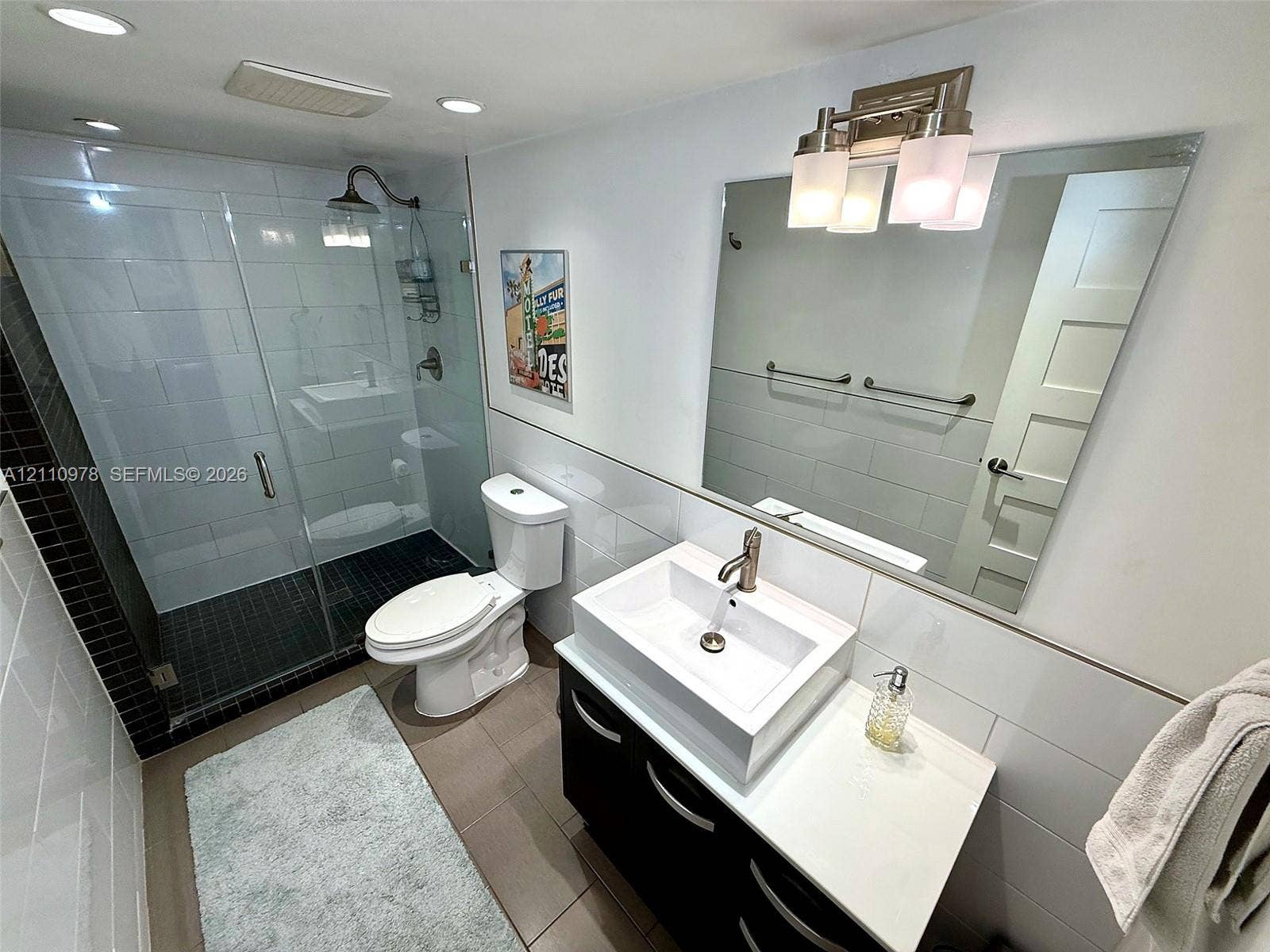 Bathroom featuring a glass-enclosed walk-in shower with tile surround, vanity with rectangular vessel sink, polished metal faucet, built-in cabinetry, and wall-mounted vanity lighting