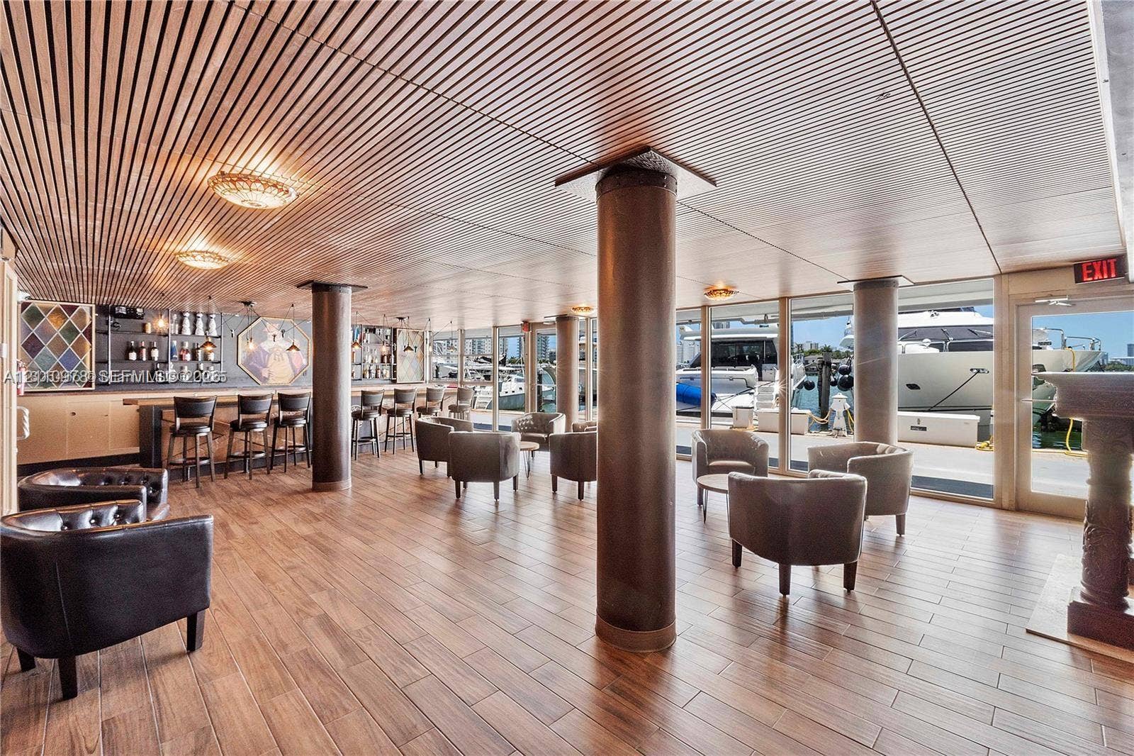 900 Bay Drive, #225, Miami Beach, FL 33141 Custom bar area featuring wood-finish flooring, slatted wood ceiling, cylindrical support columns, and floor-to-ceiling glass paneling