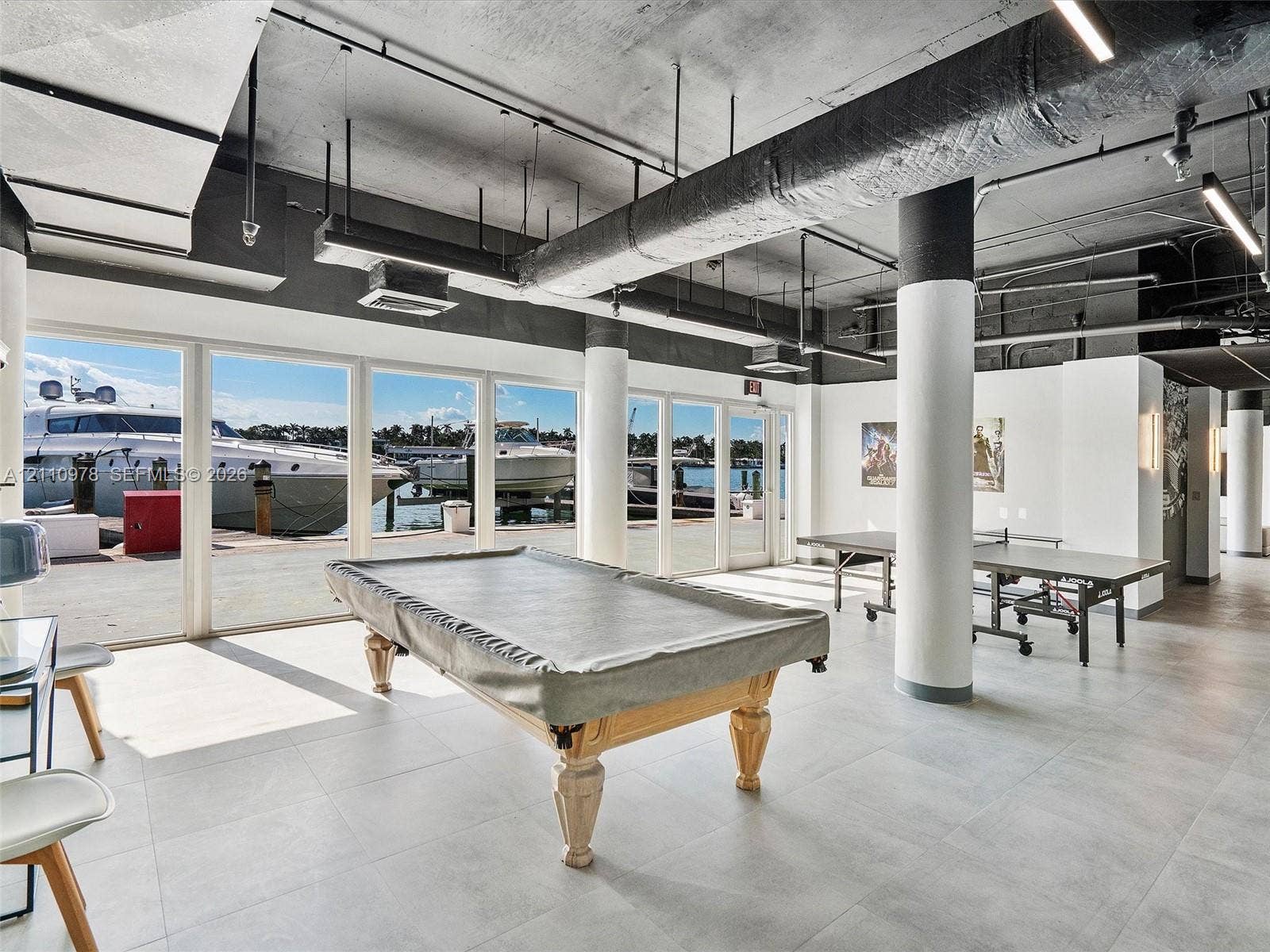 900 Bay Drive, #225, Miami Beach, FL 33141 Industrial-style interior featuring a concrete ceiling with exposed ductwork, large-format tile flooring, floor-to-ceiling glass panel walls, and cylindrical structural columns