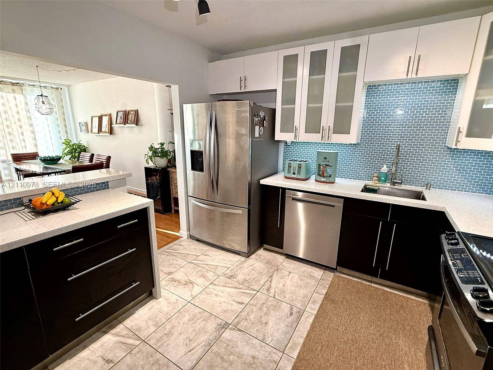Kitchen featuring two-tone cabinetry, stainless steel appliances, quartz countertops, blue glass tile backsplash, and ceramic tile flooring