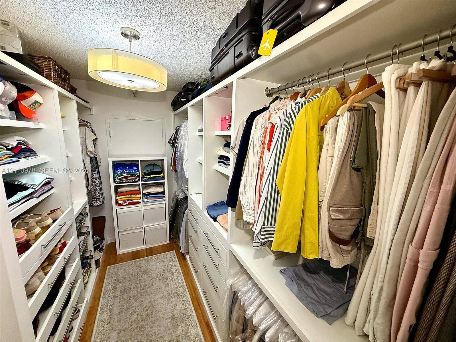 Walk-in closet featuring white built-in shelving, integrated dresser drawers, multi-level hanging rods, and a drum-style ceiling light fixture