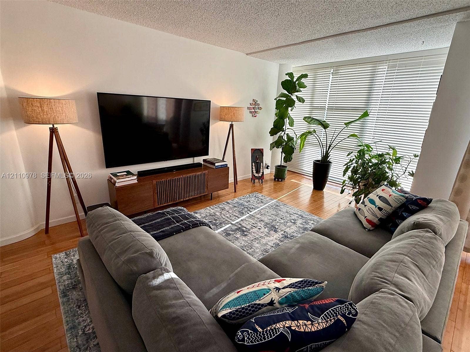 Living area featuring wood-finish flooring and large windows with horizontal blinds