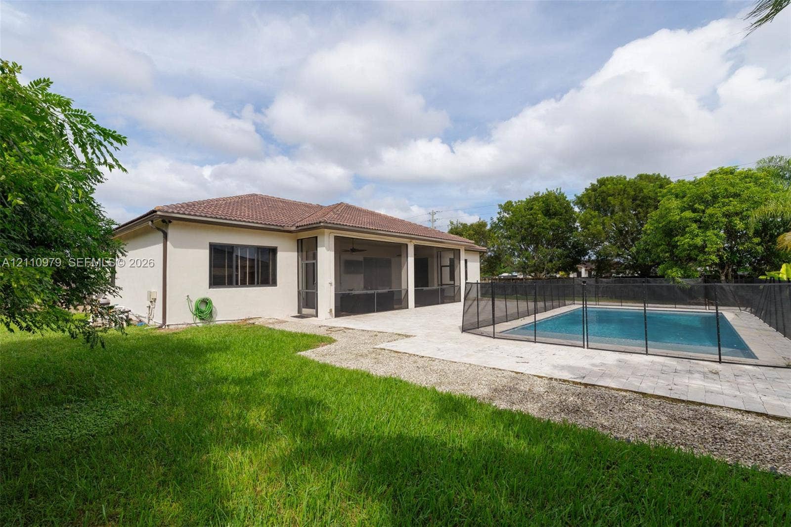 Stucco exterior featuring a screened-in lanai, concrete paver patio, in-ground swimming pool with safety fencing, and a manicured lawn
