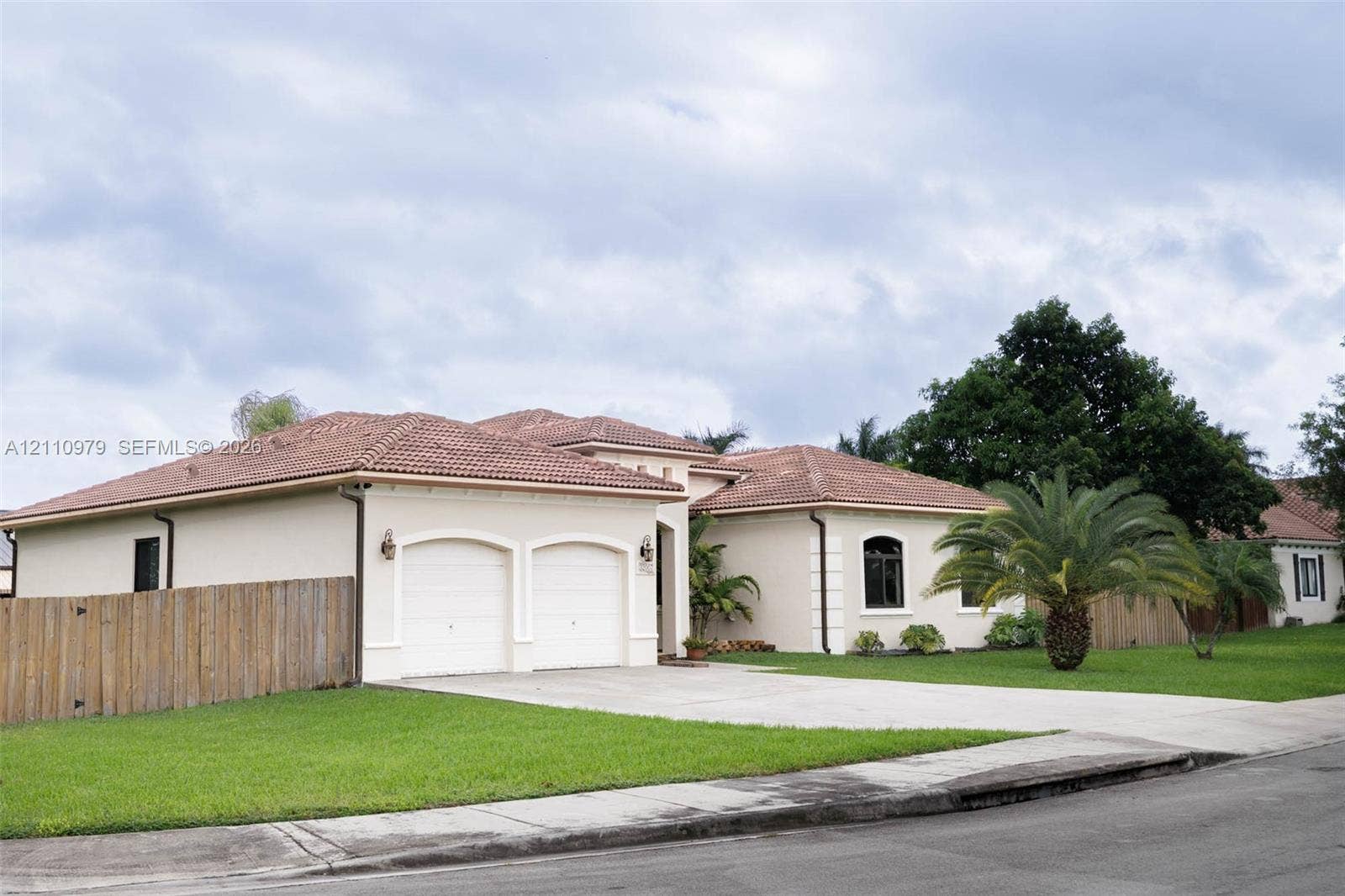 Stucco exterior with a tiled roof, two-car garage, concrete driveway, and manicured landscaping