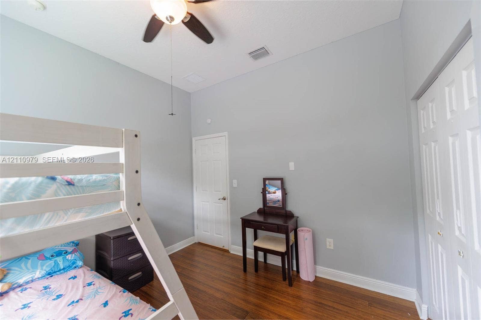 High-ceilinged room featuring wood-finish flooring, a ceiling fan with integrated lighting, a solid-core interior door, and a multi-panel closet door