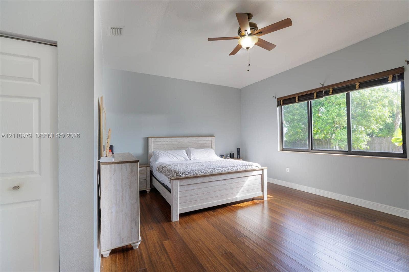 Spacious room featuring wood-finish flooring, a ceiling fan with integrated lighting, and large windows with dark-finish trim